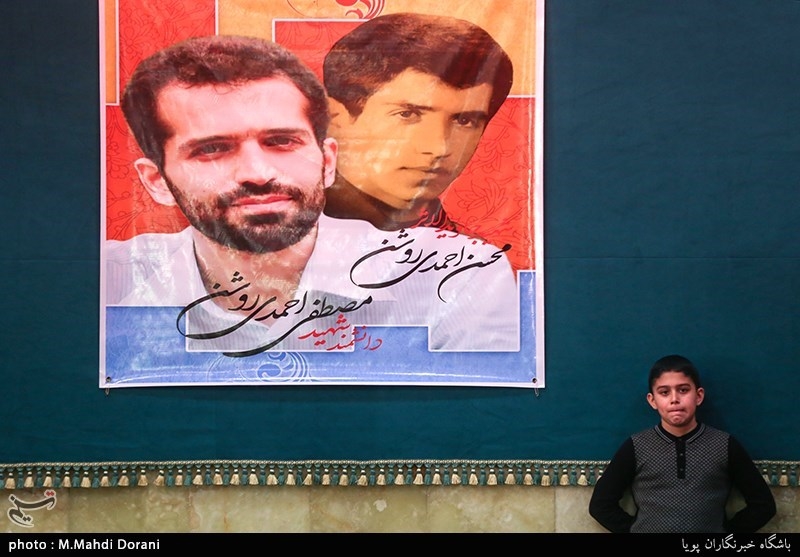 علیرضا احمدی روشن در کنار پوستر پدر