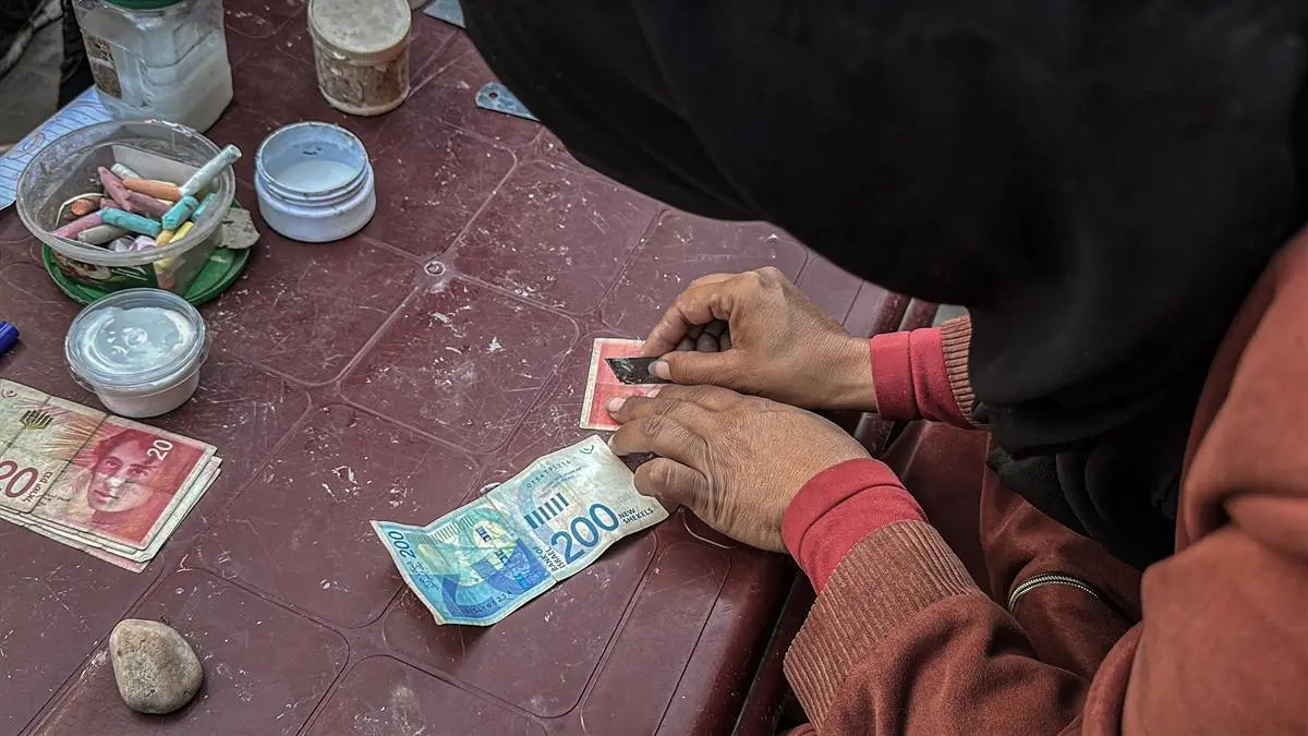 تصاویر زن فلسطینی که با ترمیم اسکناس‌های پاره امرار معاش می‌کند!