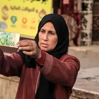تصاویر زن فلسطینی که با ترمیم اسکناس‌های پاره امرار معاش می‌کند!